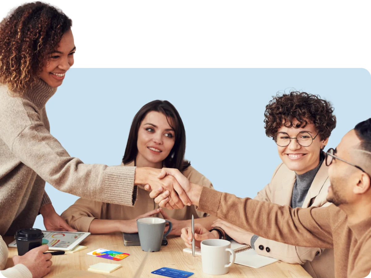 Gruppo di persone in riunione attorno a un tavolo mentre si stringono la mano durante un incontro di lavoro